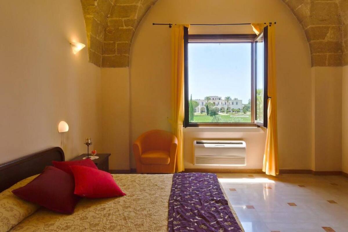 A bedroom with a bed, a nightstand, a chair, and a window with curtains.