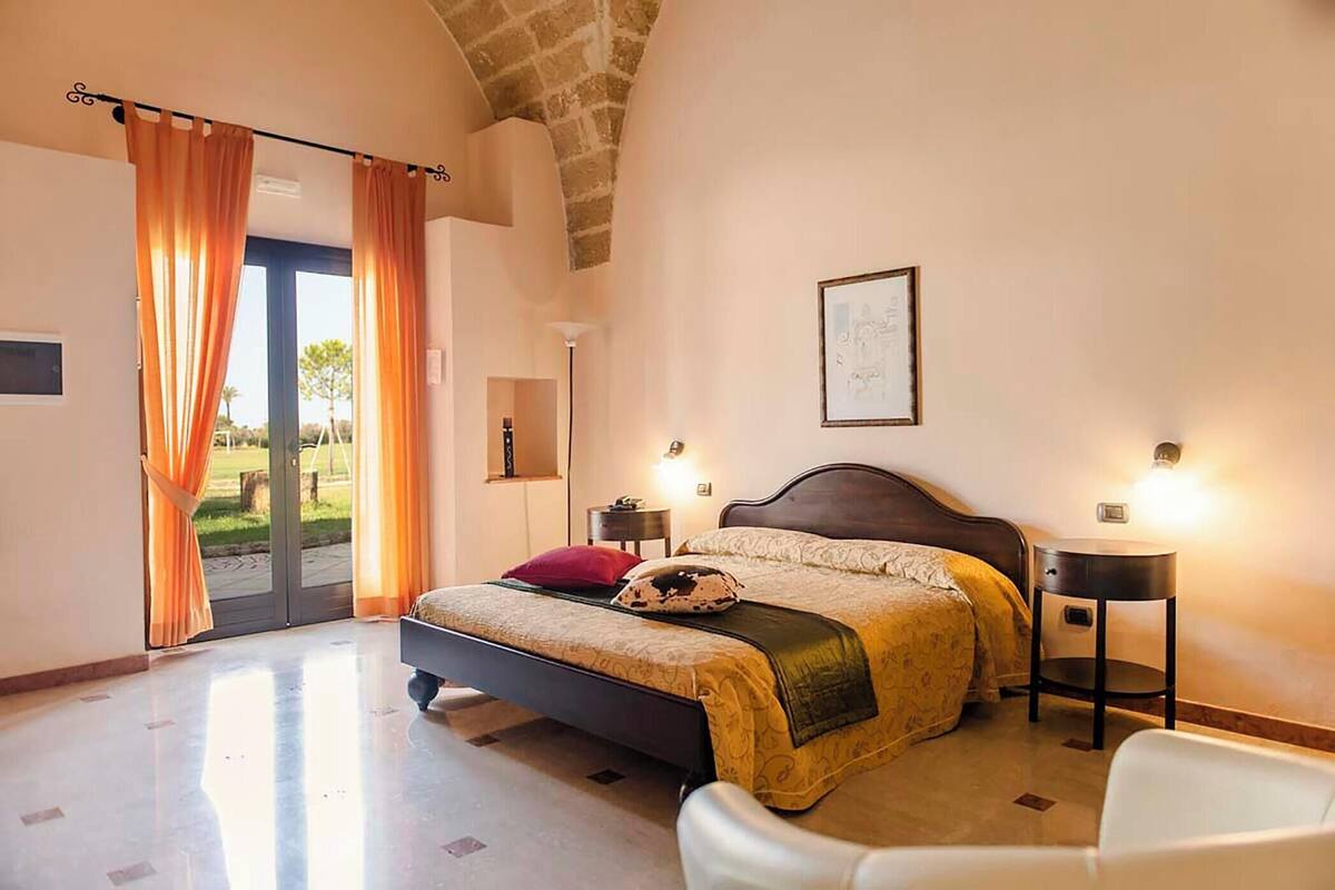 A bedroom with a bed, a chair, a bedside table, a lamp, and a door leading to a balcony.