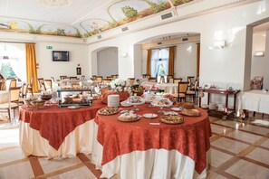 A banquet hall with round tables covered in red and white tablecloths, decorated with various dishes and a floral centerpiece. - Masseria la Baronessa Resort (Tuglie)