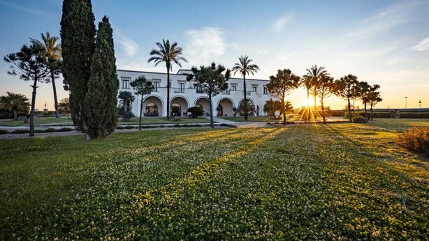 A building with a symmetrical facade, arched windows, and a central courtyard with a lawn and trees. - Masseria la Baronessa Resort (Tuglie)