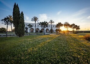 Un edificio con fachada simétrica, ventanas en arco y un patio central con césped y árboles.