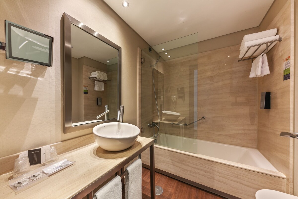 A modern bathroom with a large mirror, a round sink, a glass-enclosed shower, and a towel rack.