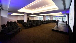 Ein Konferenzraum mit Reihen von Stühlen, einem Rednerpult und einer großen Deckenleuchte.