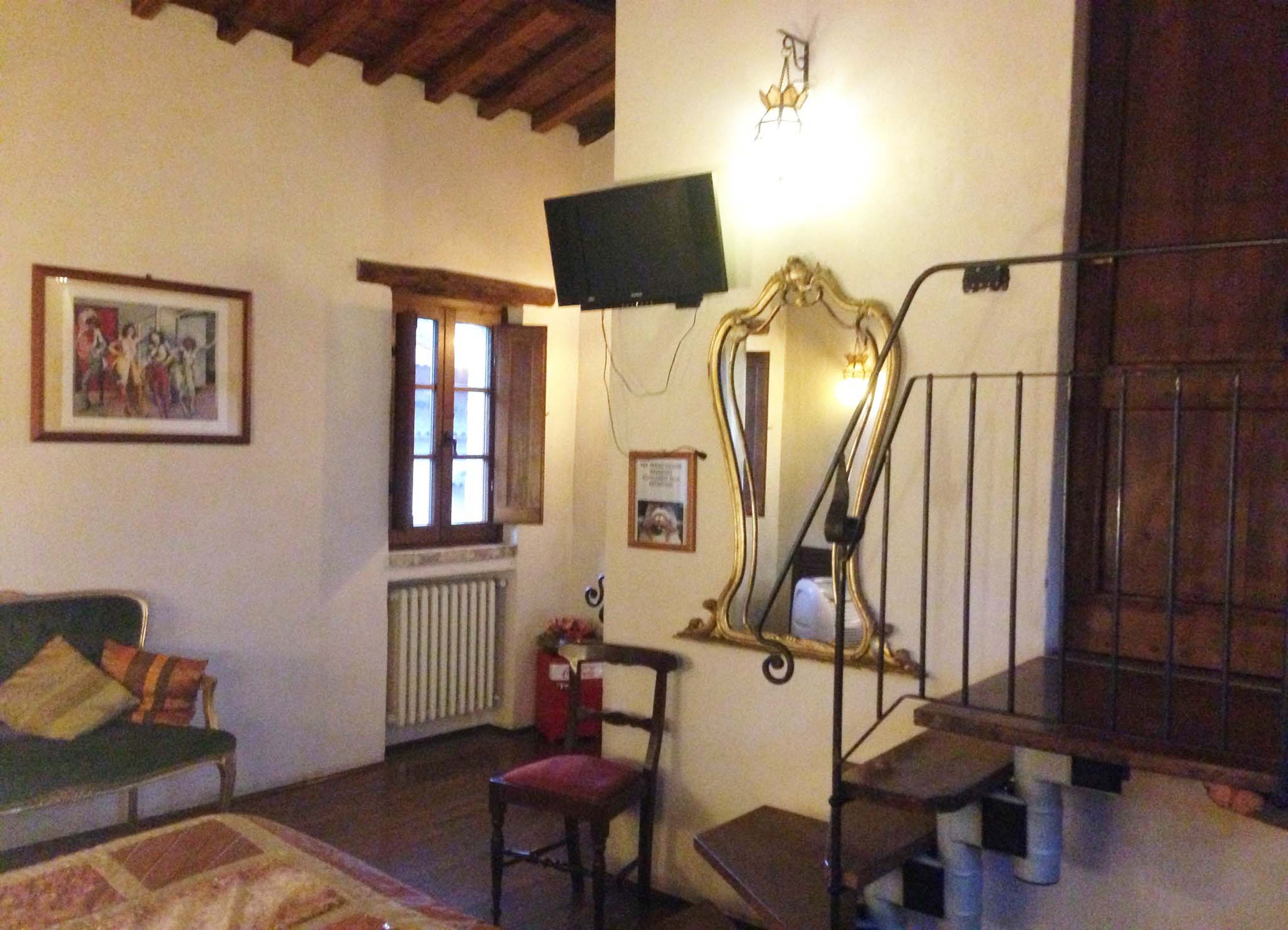 Een gezellige woonkamer met een groene bank, een rode fauteuil, een trap, een aan de muur bevestigde televisie en een raam met houten luiken.