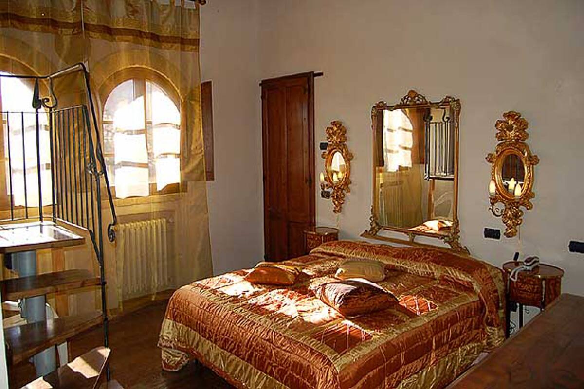Ein Schlafzimmer mit einem großen Bett, einem Holzschrank, einem Spiegel und einem Fenster mit Vorhängen.