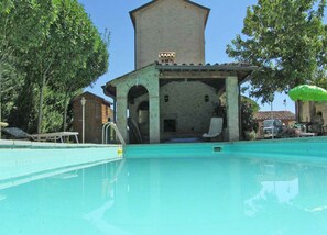 A swimming pool with a covered area, lounge chairs, and a building with a tower in the background.