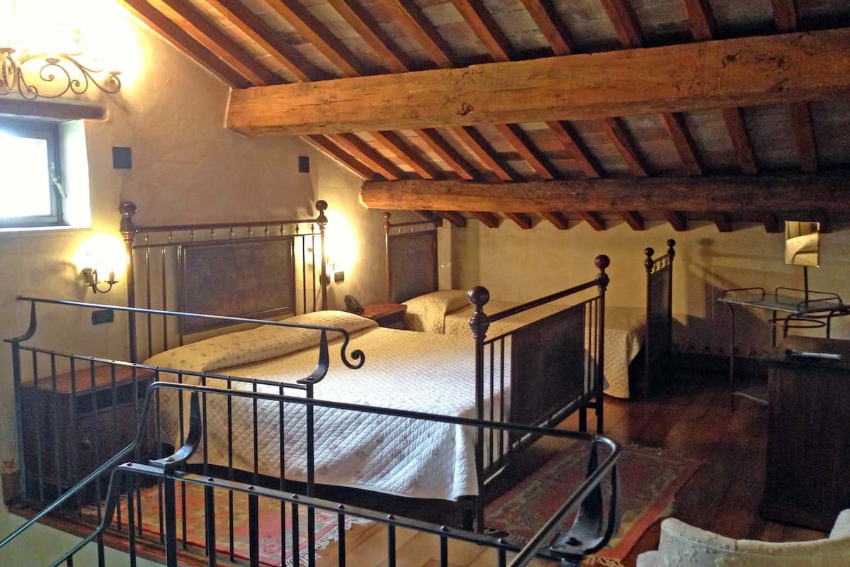 Ein rustikales Schlafzimmer mit Holzbalkendecke, einem Bett mit Metallgestell, einem Nachttisch und einem kleinen Tisch mit Lampe.