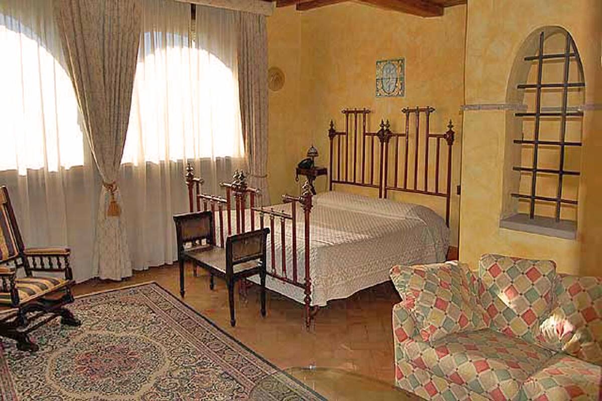 Ein Schlafzimmer mit einem Holzbett, zwei Stühlen, einem Sofa und einem großen Fenster mit Vorhängen.