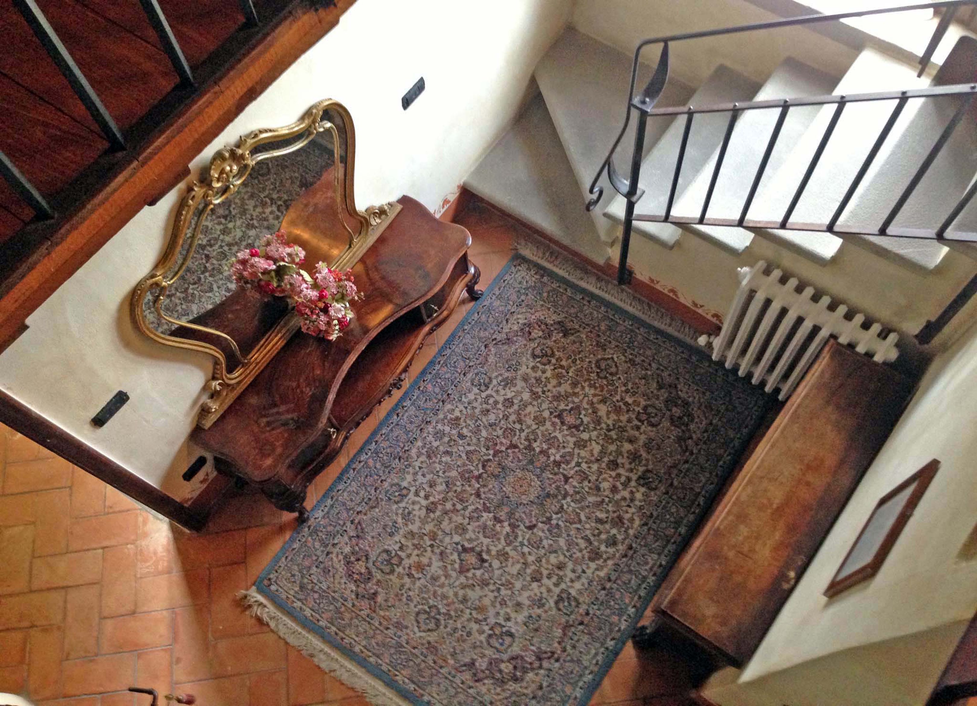 Una scala con ringhiera in metallo, un tappeto decorato e una panca di legno con un vaso di fiori.