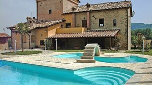 Un espace piscine comprenant deux piscines, des marches en pierre menant à l’eau, et un bâtiment avec un toit en tuiles en arrière-plan.