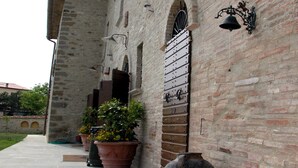 Une cour avec un mur en pierre, des plantes en pot, un grand pot en céramique et une cloche en métal.