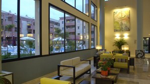 A spacious lobby with a seating area, large windows, and a view of the outdoor courtyard. - Apartamentos Leo Punta Umbría (Punta Umbría)