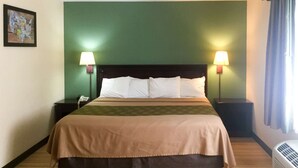 Una habitación de hotel con una cama grande, dos lámparas de noche, una mesita de noche con un teléfono y un aire acondicionado de pared.