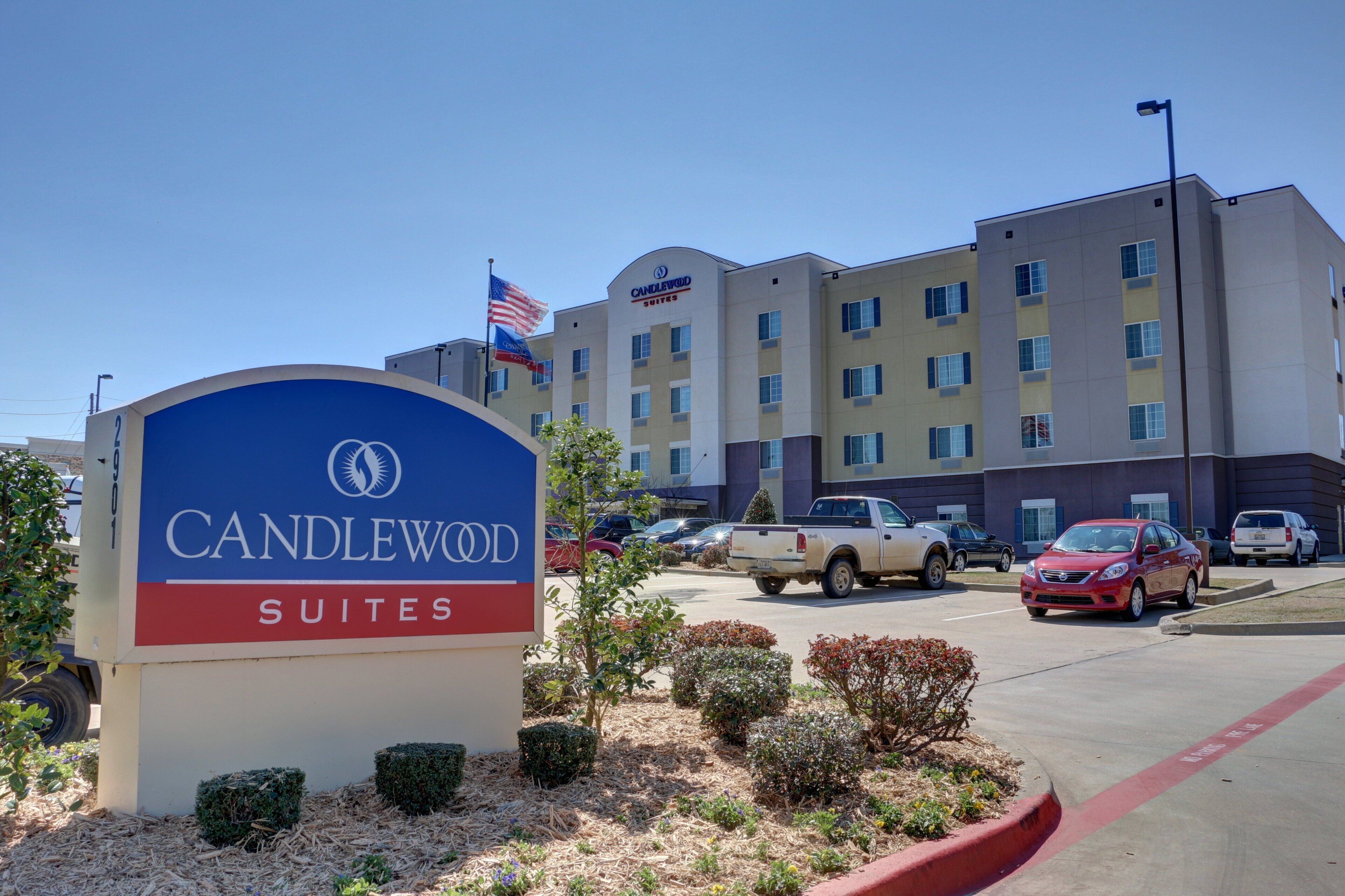 A hotel sign with a flag, a parking lot with cars, and a building with multiple windows.