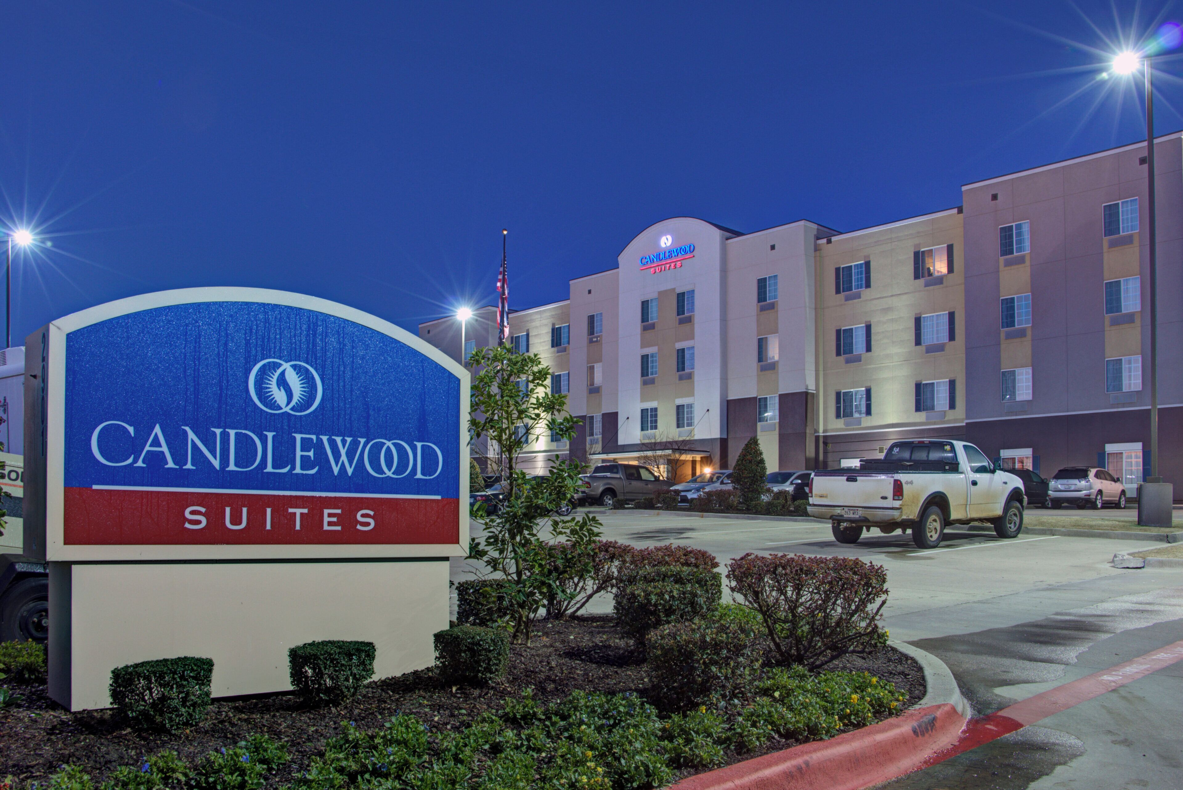 Un cartel de hotel con 'CANDLEWOOD SUITES' y un edificio con múltiples ventanas y una bandera.
