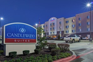 Un cartel de hotel con 'CANDLEWOOD SUITES' y un edificio con múltiples ventanas y una bandera.