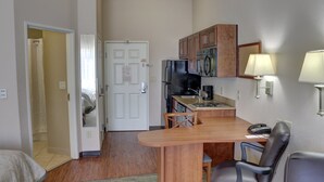 A compact kitchen with a refrigerator, microwave, and wooden cabinets. There is a small dining area with a table and chairs.