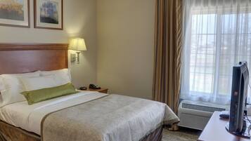 A hotel room with a bed, a desk with a computer, a lamp, and a window with curtains.