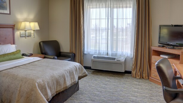 A hotel room with a bed, a desk with a computer, a chair, a TV, and a window with curtains.