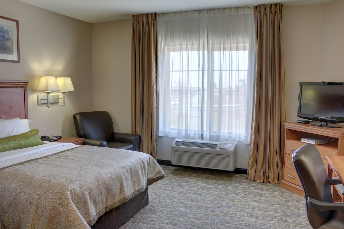Une chambre d’hôtel avec un lit, un bureau équipé d’un ordinateur, une chaise, une télévision et une fenêtre avec des rideaux.