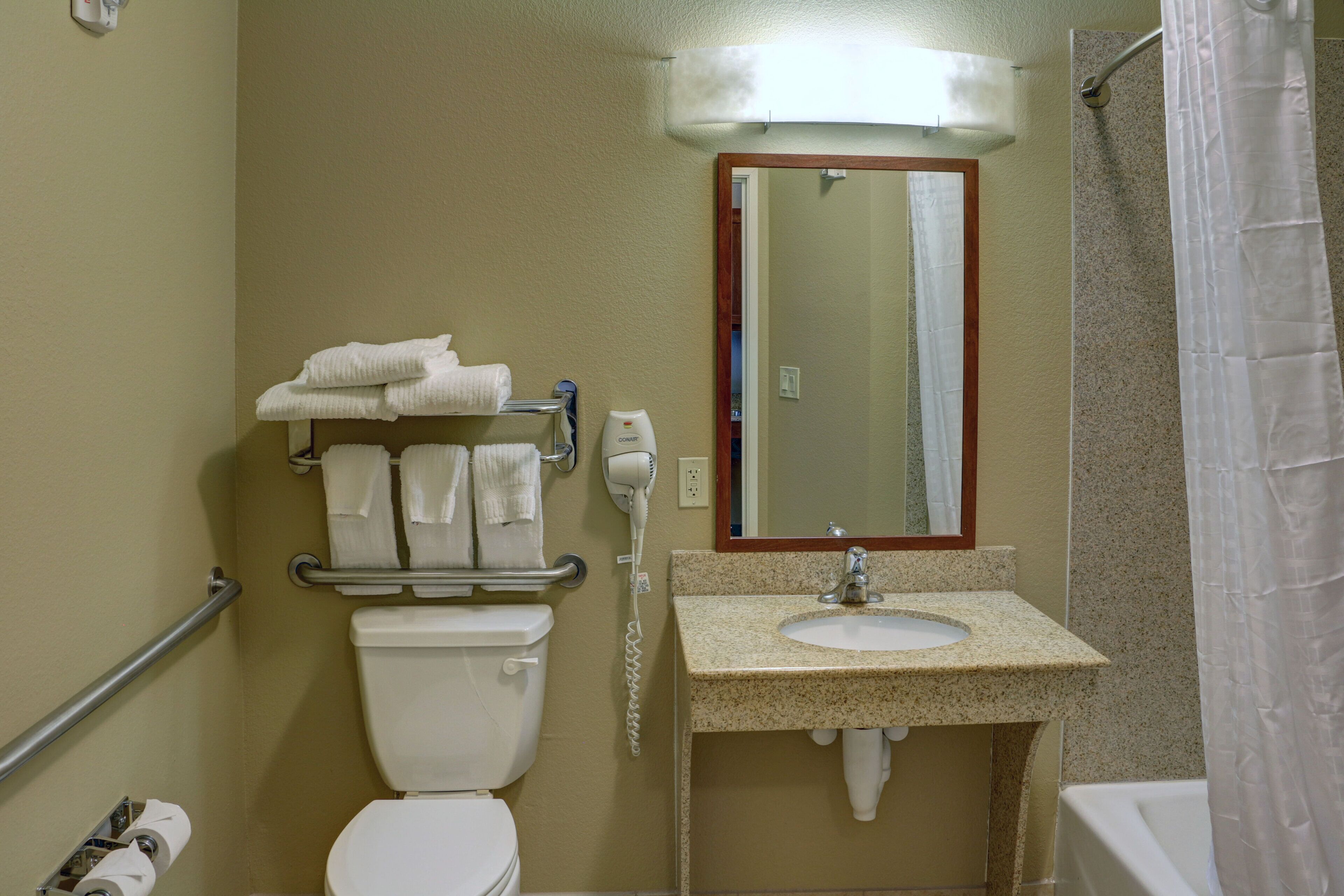 Un baño con inodoro, lavamanos, toallero y espejo.