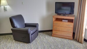 Une chambre d’hôtel avec un fauteuil en cuir, une commode en bois et un téléviseur à écran plat, ainsi qu’une lampe fixée au mur.