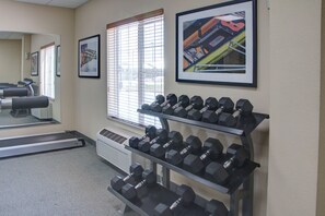 Uma academia com equipamentos de ginástica, incluindo esteiras e halteres, e quadros decorativos nas paredes.