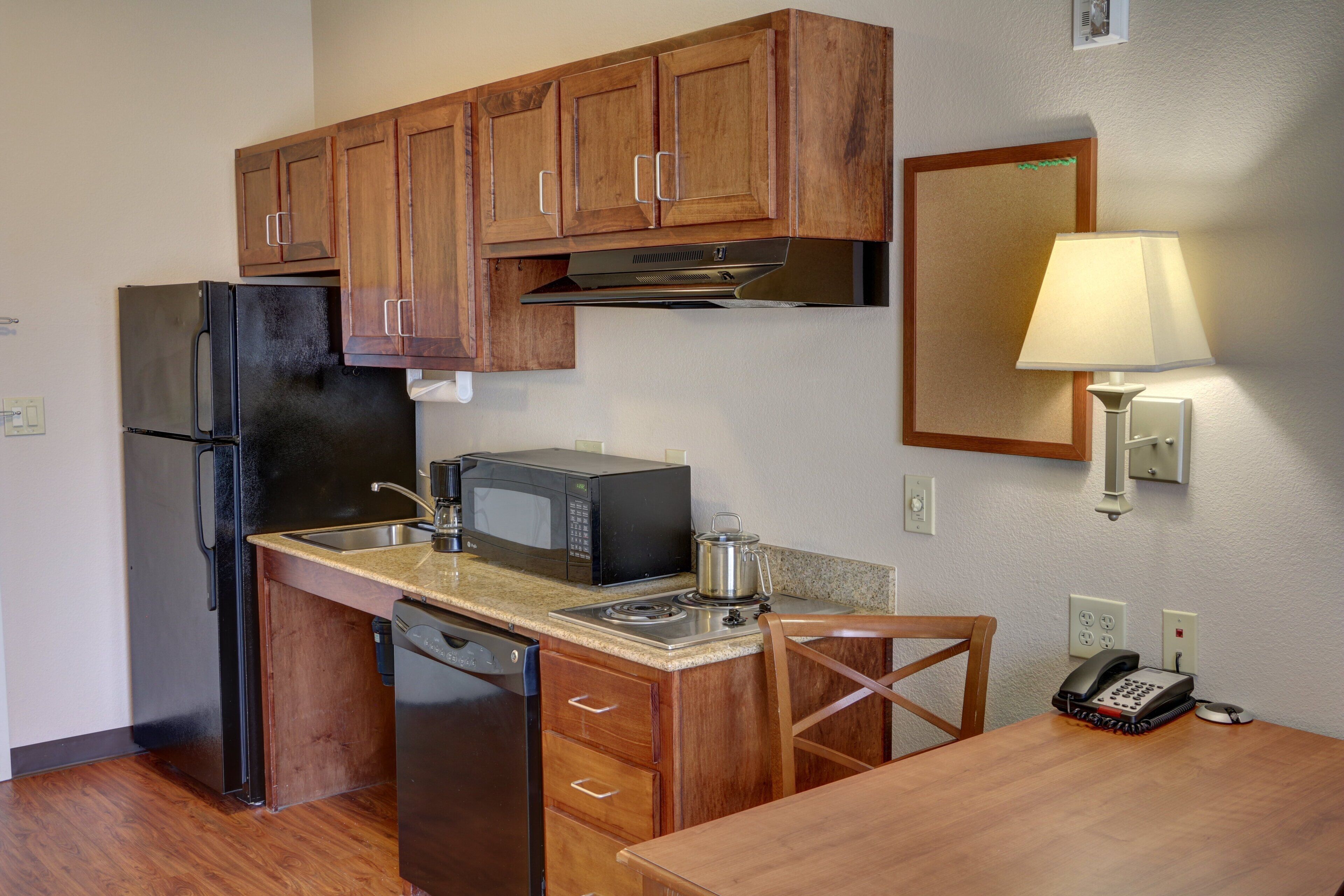 A compact kitchen with wooden cabinets, a refrigerator, a microwave, a stove, and a sink.