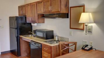 A compact kitchen with wooden cabinets, a refrigerator, a microwave, a stove, and a sink.