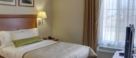 Une chambre d’hôtel avec un lit, un bureau avec un ordinateur, une lampe et une fenêtre avec des rideaux.