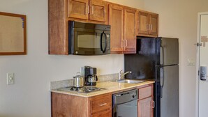 A compact kitchen with wooden cabinets, a stainless steel refrigerator, a microwave, a coffee maker, and a dishwasher.