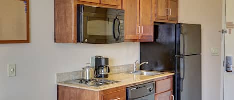 A compact kitchen with wooden cabinets, a stainless steel refrigerator, a microwave, a coffee maker, and a dishwasher.