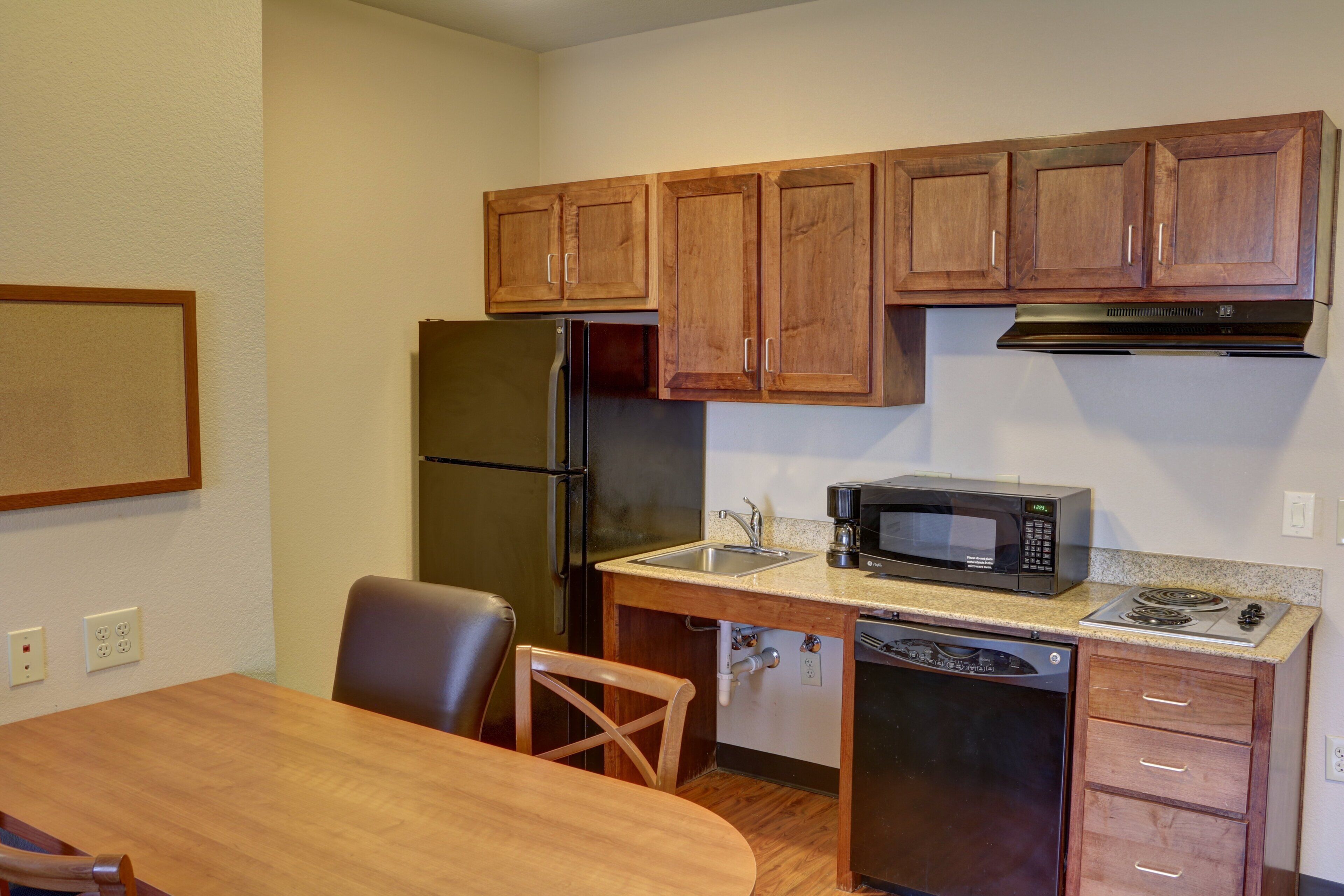 A compact kitchen with wooden cabinets, a refrigerator, a microwave, a sink, and a dishwasher.