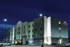 Un hotel de varios pisos con el letrero 'Candlewood Suites', un estacionamiento con varios autos y un cielo despejado.