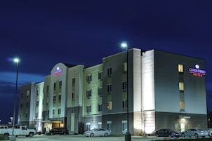 Un hotel de varios pisos con el letrero 'Candlewood Suites', un estacionamiento con varios autos y un cielo despejado.