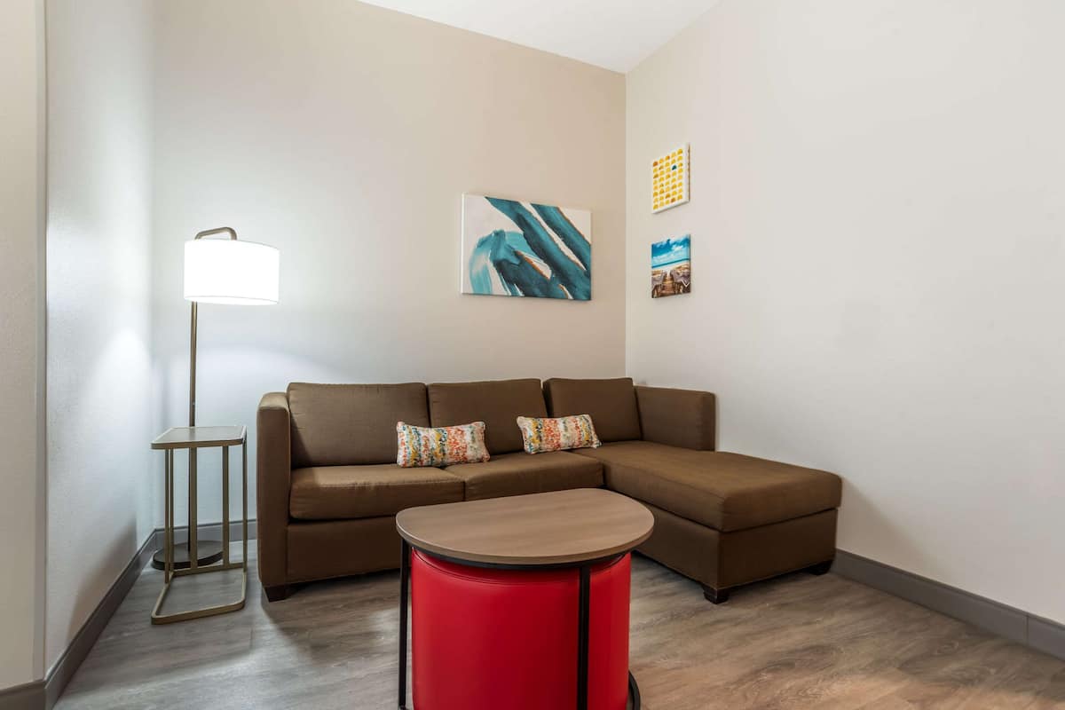 A modern living room with a brown sectional sofa, a red round table, and a floor lamp.