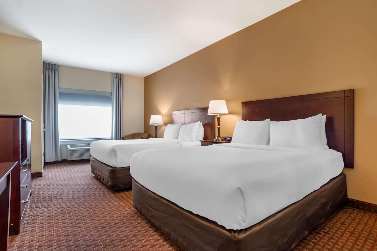 A hotel room with two beds, a dresser, and a large window with curtains.