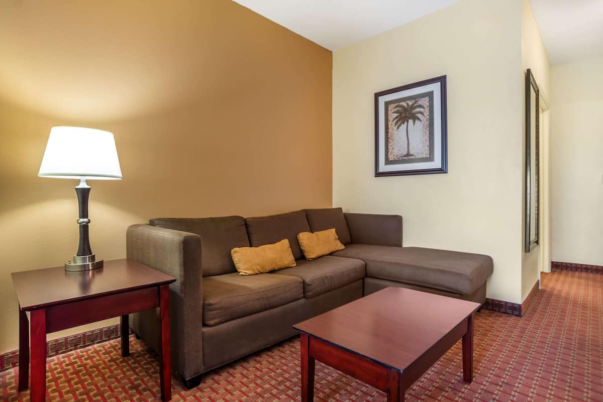 A hotel room with a brown sofa, a wooden coffee table, a lamp, and a framed picture on the wall.