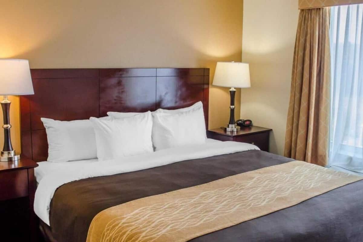 A hotel room with a large bed, two bedside tables with lamps, a headboard, and a window with curtains.