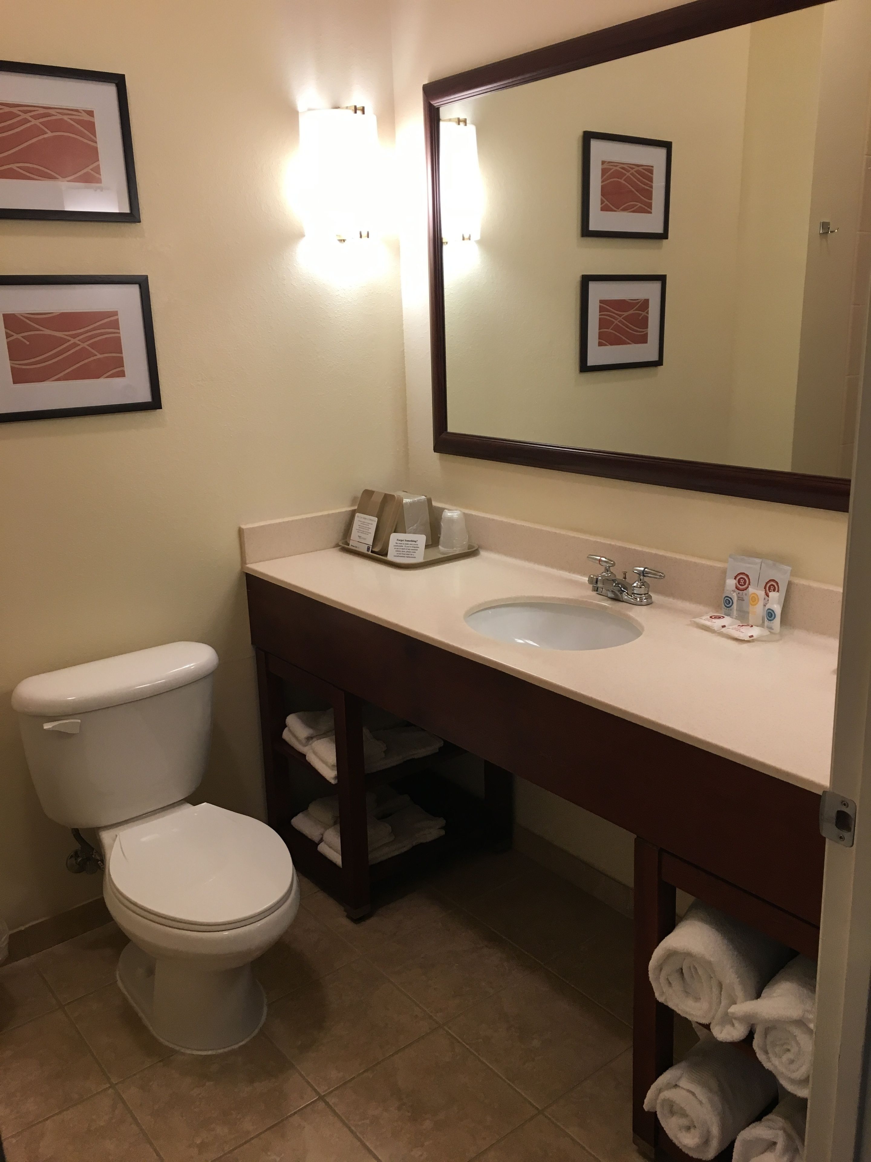 A bathroom with a toilet, sink, and mirror. There are towels and toiletries on the counter.