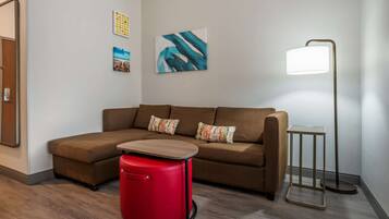 A modern living room with a brown sectional sofa, a red ottoman, a floor lamp, and abstract wall art.