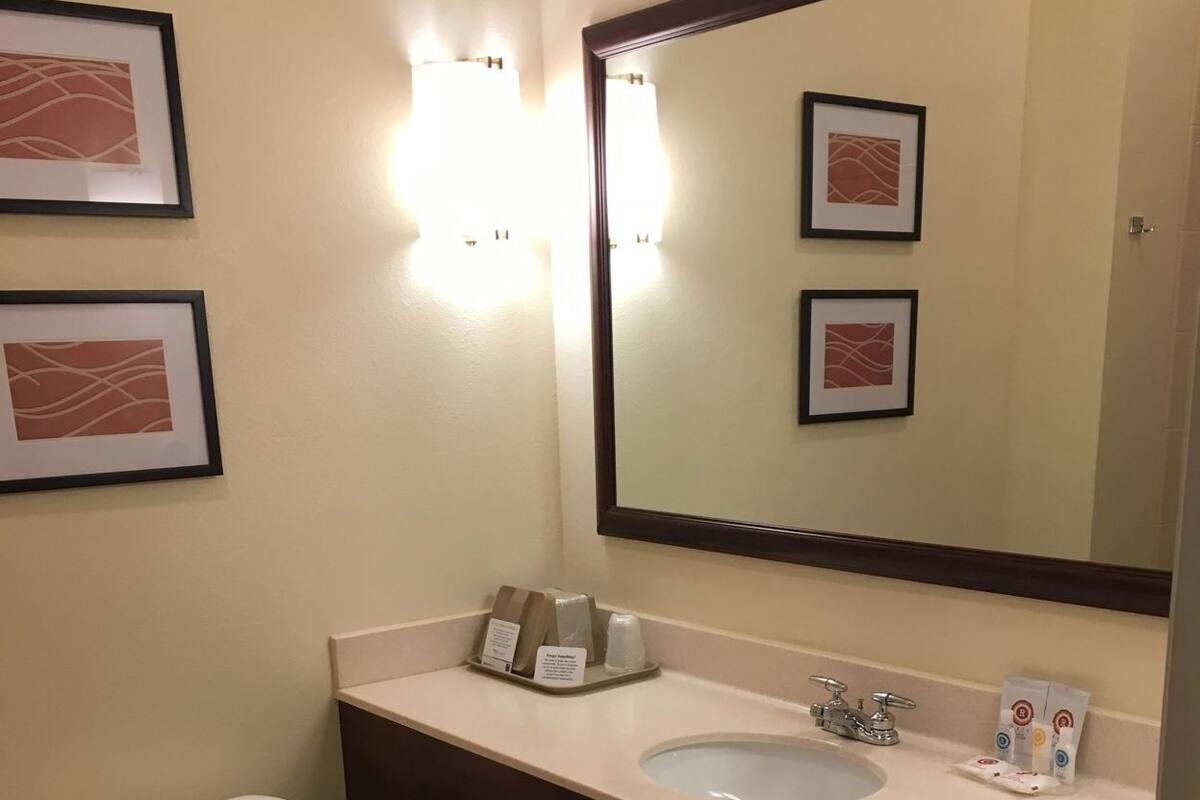 A bathroom with a toilet, sink, and mirror. There are towels and toiletries on the counter.