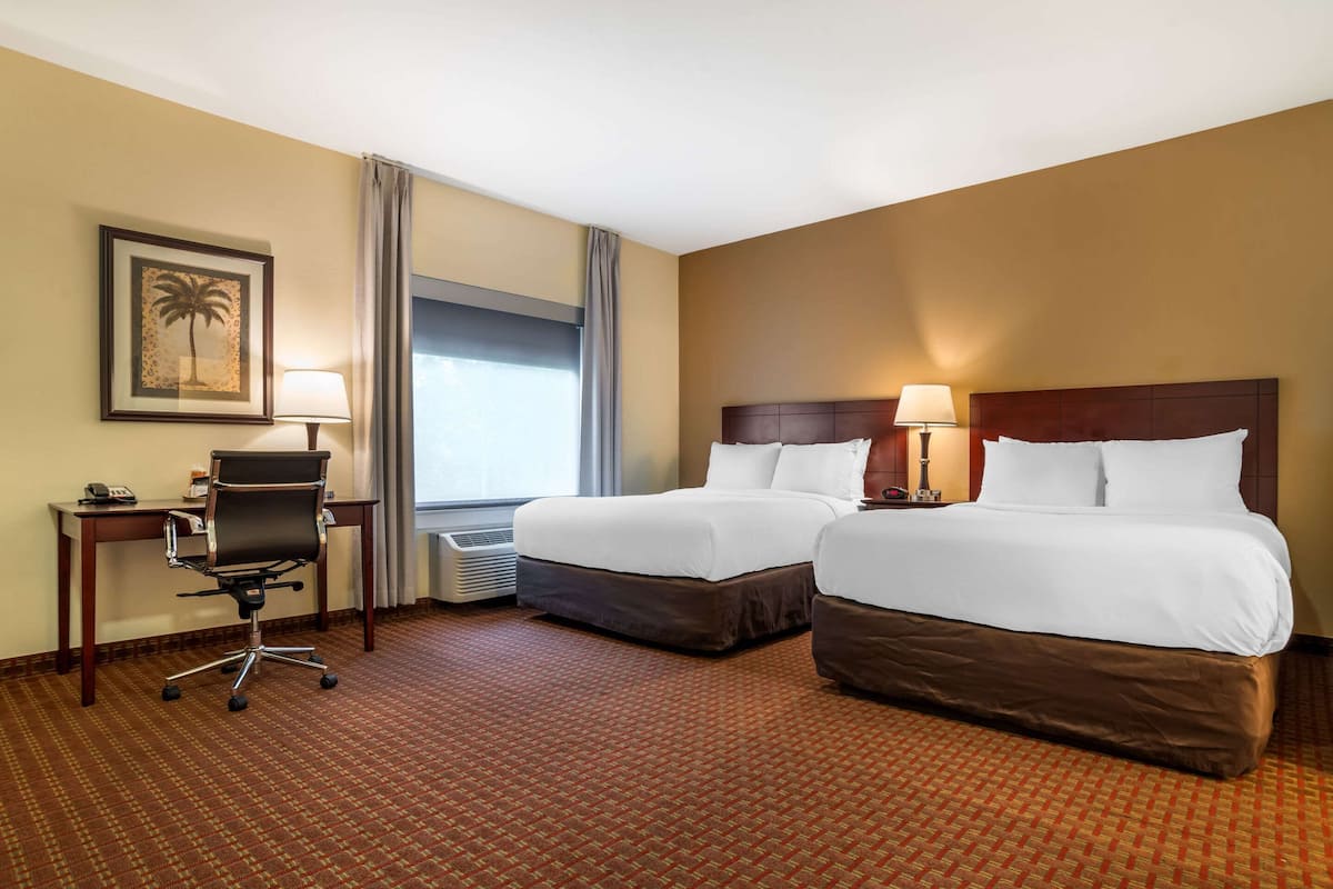 A hotel room with two beds, a desk with a chair, a framed picture on the wall, and a window with curtains.