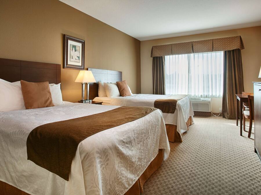 A hotel room with two beds, a desk, a dresser, a TV, and a window with curtains.