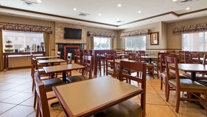 A restaurant with multiple wooden tables and chairs, a flat-screen TV mounted on the wall, and a fireplace. - Best Western Plus Montezuma Inn & Suites (Las Vegas)