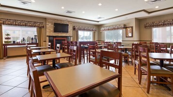 Un restaurante con varias mesas y sillas de madera, un televisor de pantalla plana en la pared y una chimenea.