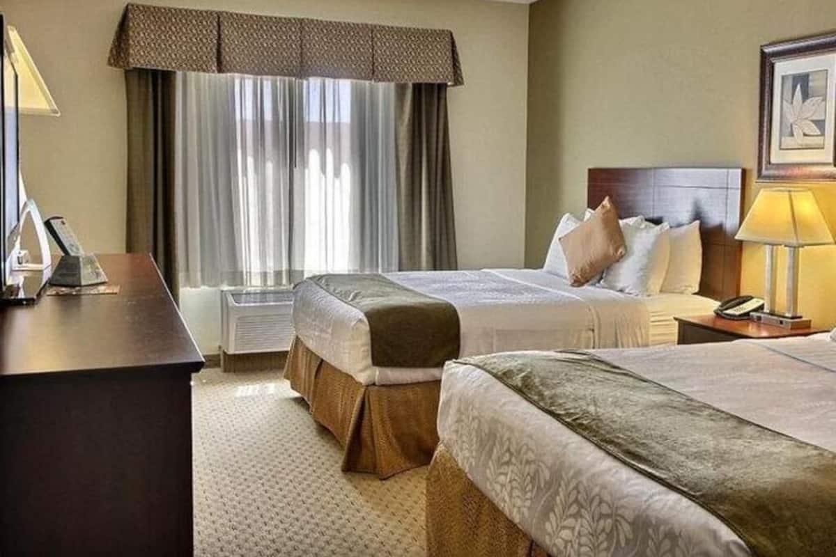 A hotel room with two beds, a desk, a telephone, and a window with curtains.