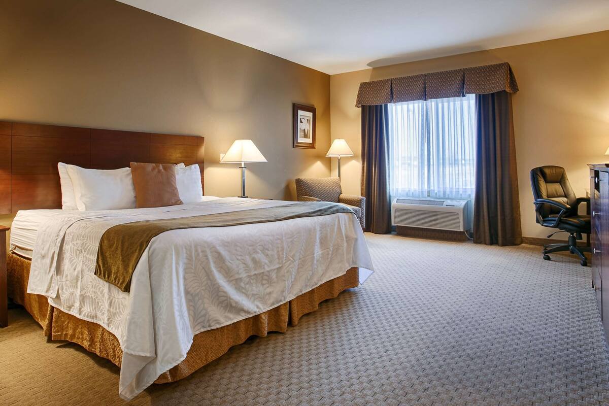 A hotel room with a large bed, two bedside lamps, a chair, a desk, and a window with curtains.