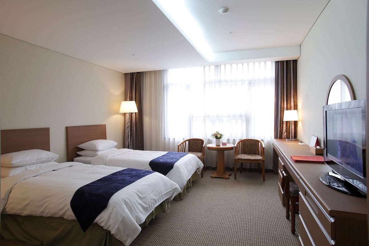 Une chambre d’hôtel avec deux lits, un bureau avec une télévision et une petite table avec des chaises.