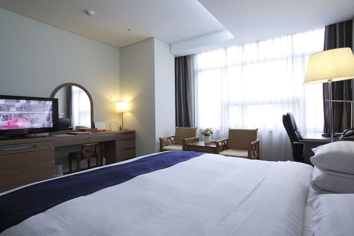 Une chambre d’hôtel équipée d’un lit, d’un bureau, d’une télévision, d’une chaise, d’une lampe et de grandes fenêtres.